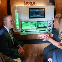 Vier Personen sitzen in einem holzvertäfelten Raum bei der zahntechnikplus um ein geöffnetes Gerät mit grün leuchtender Innenbeleuchtung und Bildschirm, während eine Frau eine Funktion erklärt.