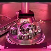 Metallbauteile für Zahnersatz stehen bei der zahntechnikplus auf einer runden Bauplattform in einer 3D-Druckmaschine unter rosafarbenem Licht.