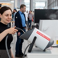 Eine Frau bedient bei der zahntechnikplus ein Dampfreinigungsgerät an einem Messestand; im Hintergrund sind weitere Personen und Geräte zu sehen.