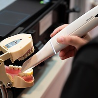 Eine Hand scannt mit einem weißen Intraoralscanner ein aufgespanntes Zahnmodell