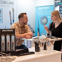 Zwei Frauen stehen an einem Messestand der zahntechnikplus und sprechen mit einem Mann hinter dem Tresen