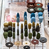 Verschieden geformte Schleifkörper und Polierscheiben in bunten Farben sind bei der zahntechnikplus geordnet in Halterungen auf einem Ausstellungstisch präsentiert.